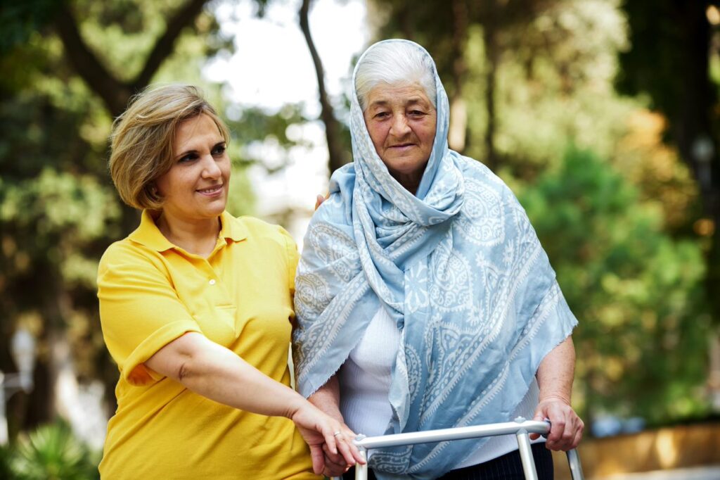 older woman using a walker with another woman helping